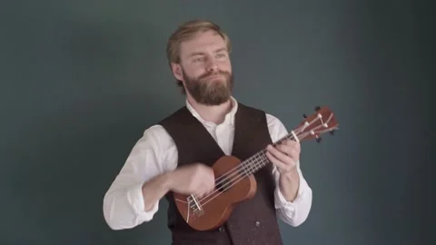 Man with a beard plays a ukulele against a green wall Stock Footage 164244346