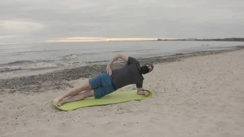Man with Beard in Protective Face Mask Performing Side Elbow Plank on Seashore Stock Footage 130727837