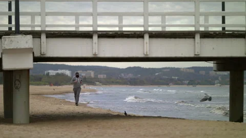 Man with Beard in Protective Face Mask Running by the Beach at Dusk - Wide Shot Stock Footage 130739242