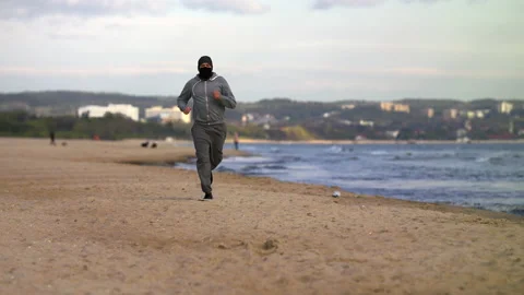 Man with Beard in Protective Face Mask Running by the Beach at Dusk - Wide Shot Stock Footage 130849817