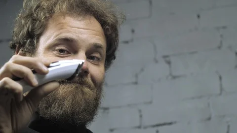 A man with a beard shaves his head with an electric trimmer. man in barbershop Stock Footage 120500670