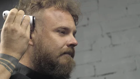 A man with a beard shaves his head with an electric trimmer. bearded hipster Stock Footage 120559731
