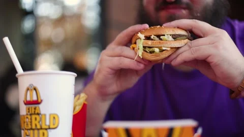 Man with beard sits at McDonald's table and eats Big Mac burger Stock Footage 340428137