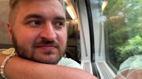 Man with beard sits on seat and looks out of large train window Stock Footage 313363010