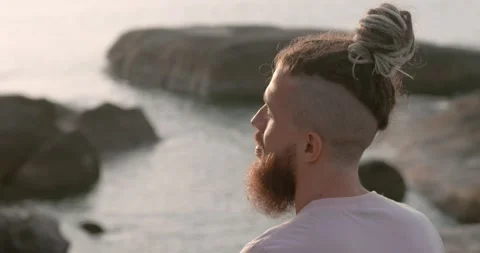 Man with beard sitting calmly on beach at sunset side view close-up Stock Footage 266860941