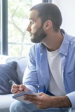Man with beard sitting on a couch, focused and thoughtfully looking away wh.. Stock Photos