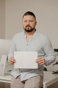 A man with a beard is sitting with an empty sheet of white paper near a compu Stock Photos