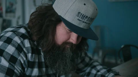 Man with beard sitting in kitchen and looking down writing Video stock 131235132