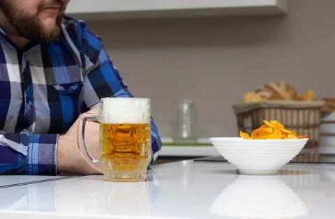 A man with a beard is sitting in the kitchen, on the table is a glass of beer Foto stock