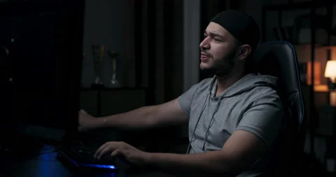 Man with beard is sitting in room and playing online games. The player in the Stock Footage 214148686