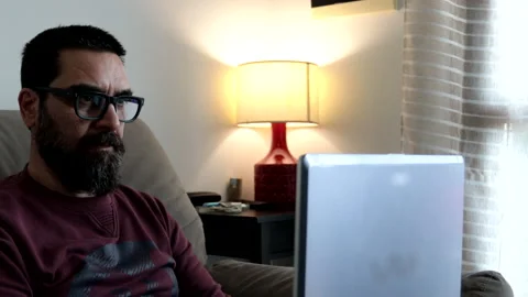 Man with beard sitting on sofa at home works with laptop pc typing on keyboard. Vídeos de archivo 239014680