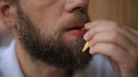 A man with a beard sitting at a table in a street cafe and eating French fries Stock Footage 99137989