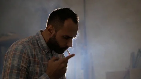 A man with a beard smokes against the background of front light Stock Footage 99578215