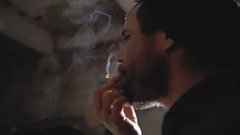 A man with a beard smokes a cigarette and produces smoke.marijuana smoking Stock Footage 102942282