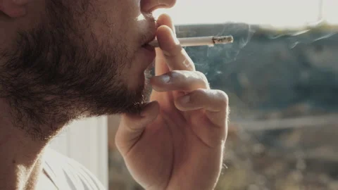 A man with a beard smokes a cigarette by the window. Smoker Aman Video stock 142245124