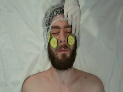 Man with a beard in a spa salon on a white sheet. A man is made a mask cucumbers Stock Footage 128705659