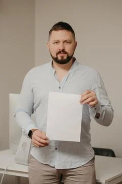 Man with a beard is standing with an empty sheet of white paper near a comput Stock Photos
