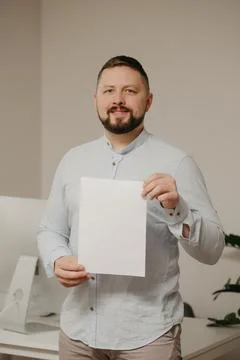 Man with a beard is standing with an empty sheet of white paper near a comput Stock Photos