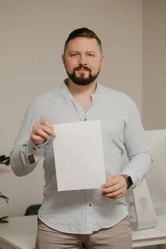 Man with a beard is standing with an empty sheet of white paper near a comput Stock Photos