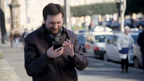 A man with a beard is standing outside looking for something in his phone Stock Footage 102276299