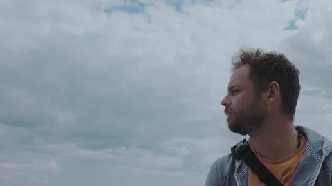 A man with a beard stands on a background of clouds near the sea. 4k video Stock Footage 115480349