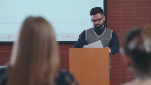 Man with beard stands behind pulpit and explains material to students Vídeo Stock 88805122
