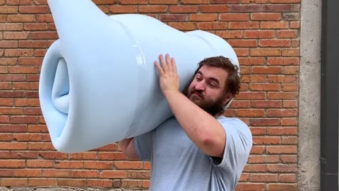 Man with beard stands near brick wall of house, holds blue foam rubber Video stock 340427585
