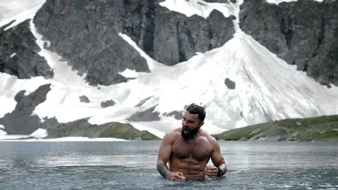 A man with a beard swims and screams in an ice lake in the highlands Stock Footage 138689890