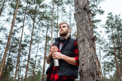 Man with beard taking rest in forest after walk, is drinking hot coffee Stock Photos