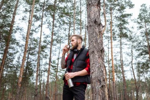 Man with beard taking rest in forest after walk, is drinking hot coffee Stock Photos