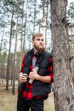 Man with beard taking rest in forest after walk, is drinking hot coffee Stock Photos