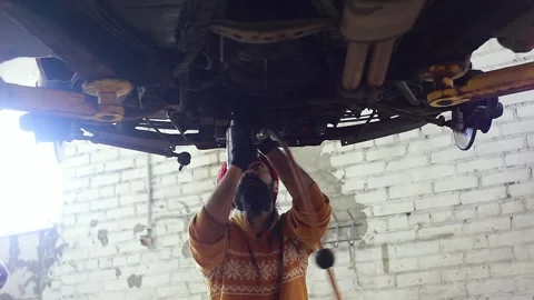 Man with a beard tightens a nut with a pneumatic wrench under the bottom of car Stock Footage 247379319