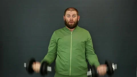 A man with a beard in a tracksuit raises his hands with heavy iron dumbbells Video stock 155759345
