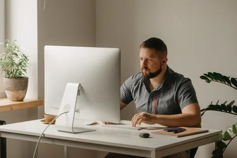A man with a beard is typing during the video conference at the desktop compu Stock Photos