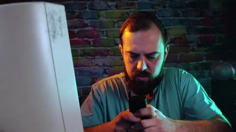 Man With Beard Typing Text Message on Flip Mobile Phone in Front of CRT Stock Footage 302173402