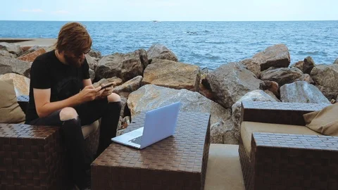 Man with beard uses cellphone in open cafe on sea beach Stock Footage 113788132