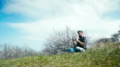 Man with a beard uses a tablet on nature near blossoming tree Stock Footage 62438782