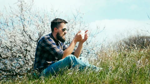 Man with a beard uses a tablet on nature near blossoming tree Stock Footage 62438822