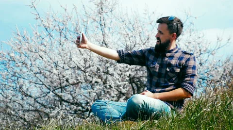 Man with a beard uses a tablet on nature near blossoming tree Stock Footage 62439068