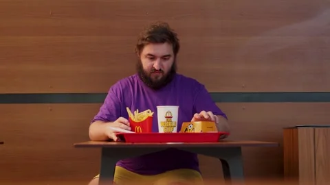 Man with beard, violet purple lilac t-shirt sits at table of McDonald's Stock Footage 340428136