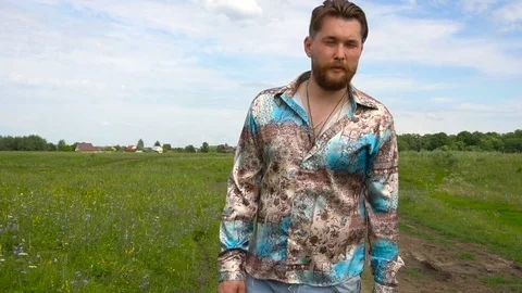 Man with beard is walking along the field on summer day Stock Footage 79600886