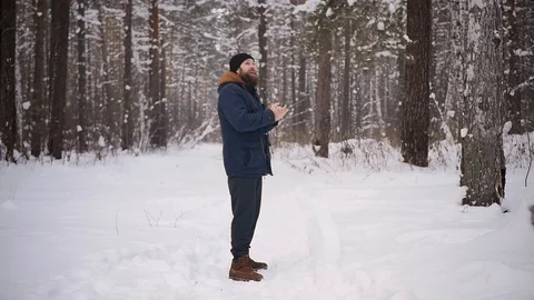 A man with a beard warms his hands near his mouth in the winter forest. Cold Stock Footage 122688273