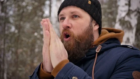 A man with a beard warms his hands near his mouth in the winter forest. Cold Stock Footage 122688348