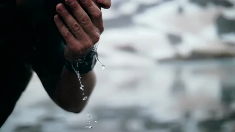 Man with a beard is washing his face in a mountain lake on top of a mountain Stock Footage 138691562
