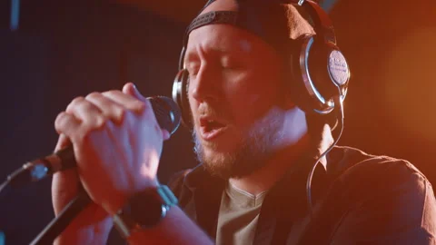 Man with a beard, wearing a cap and headphones, is laying down tracks in a music Stock Footage 273262714