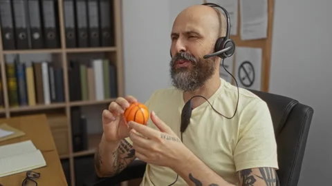 Man with beard wearing headset in office holding stress ball while talking .. Stock Footage 308568027
