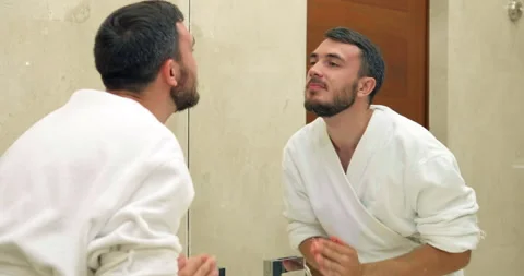 Man with beard in white bathrobe washes face in bathroom Video stock 141050630