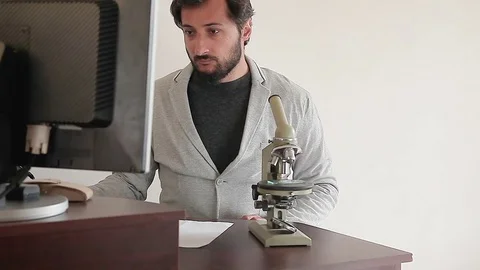 A man with a beard works with a microscope Stock Footage 75559766