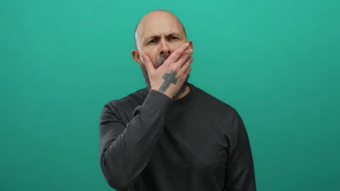 Man with a beard yawning against a solid green background, showcasing a bal.. Stock Footage 313037536