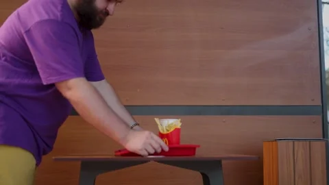 Man with beard, yellow shorts and purple t-shirt places red tray with food Vídeos de archivo 338312872